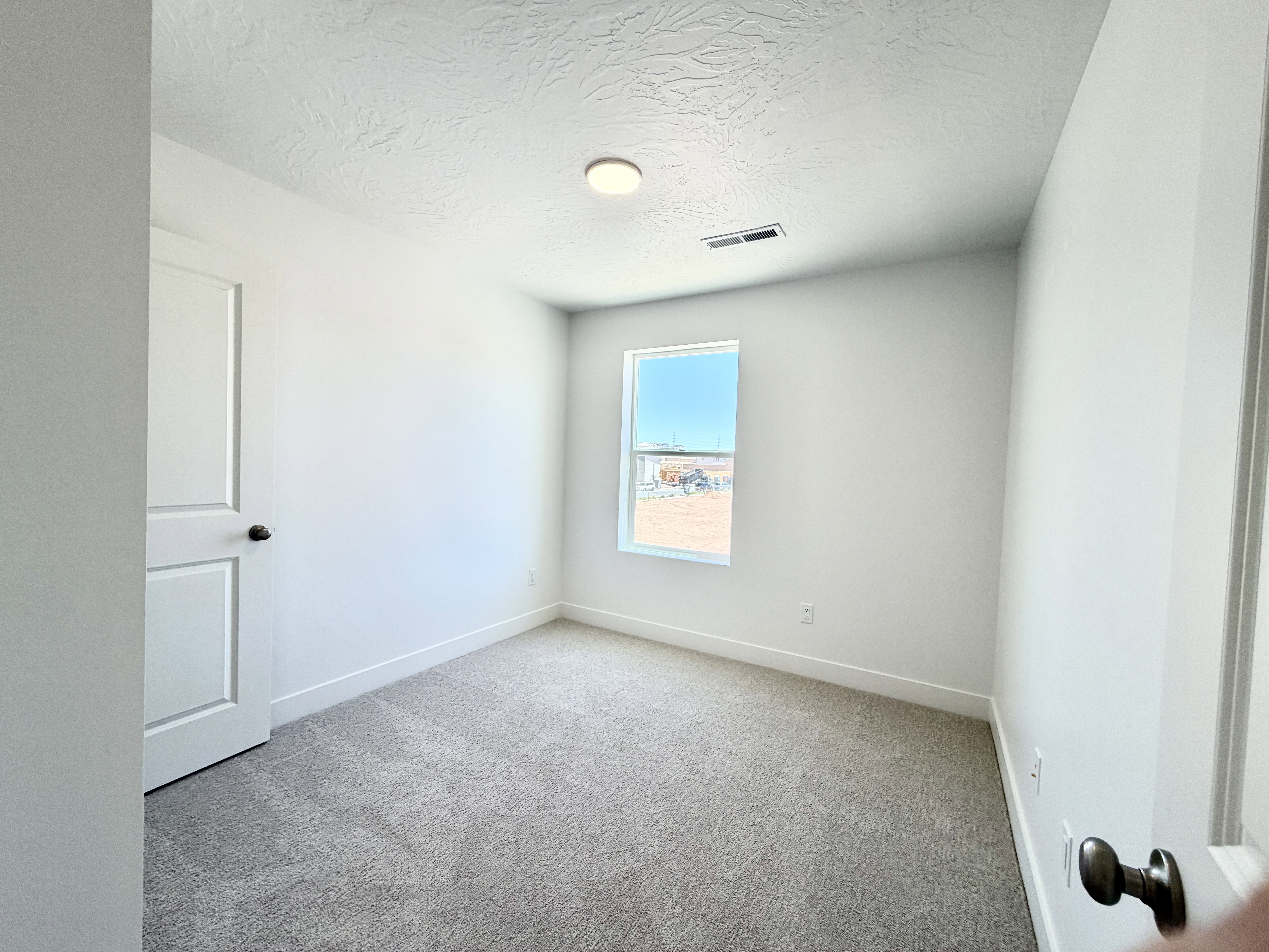 Neutral-toned carpeting extends throughout this room, featuring white walls and a single window