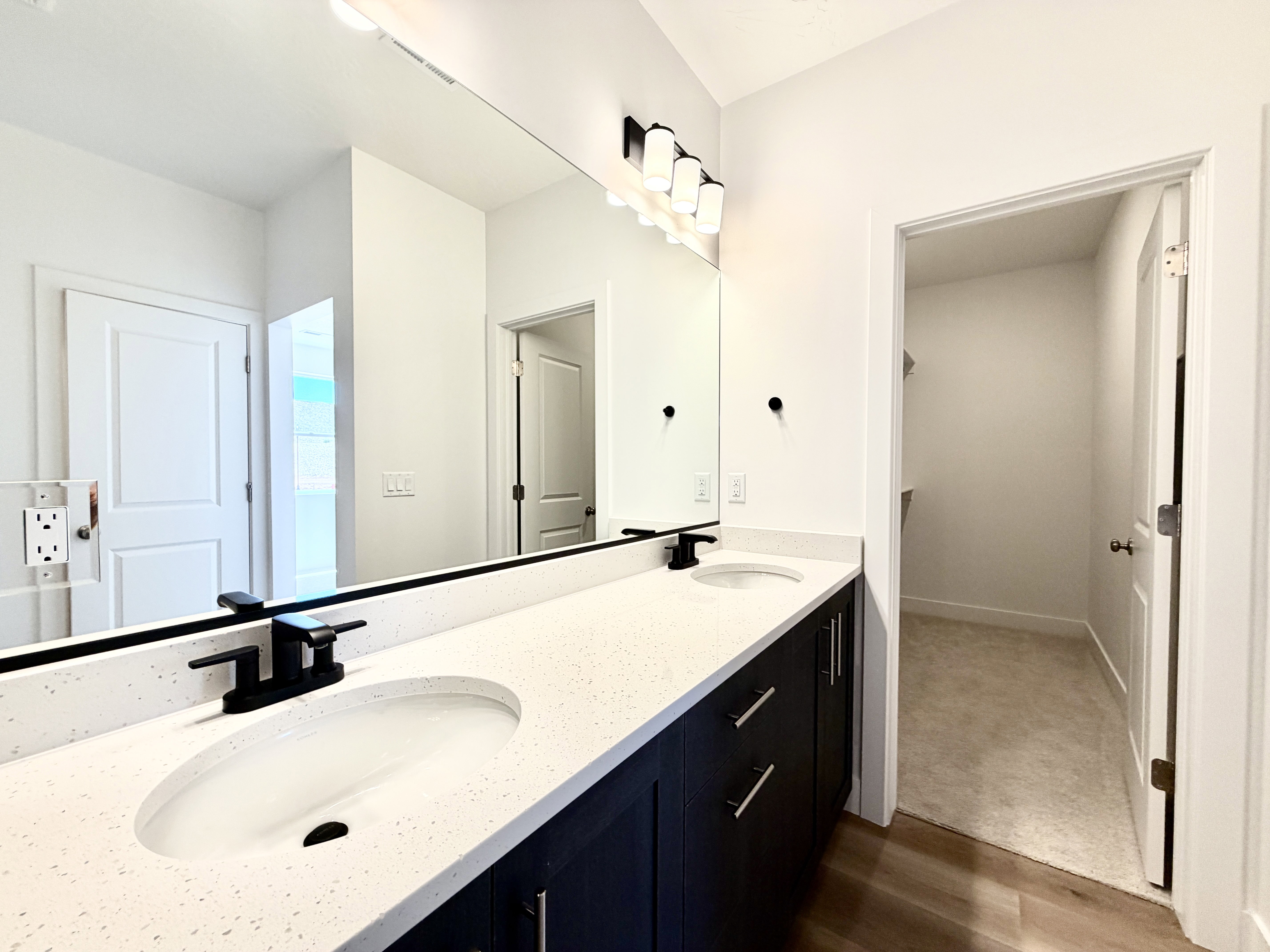 Double vanity featuring white countertops with integrated sinks, matte black faucets, and dark cabinetry
