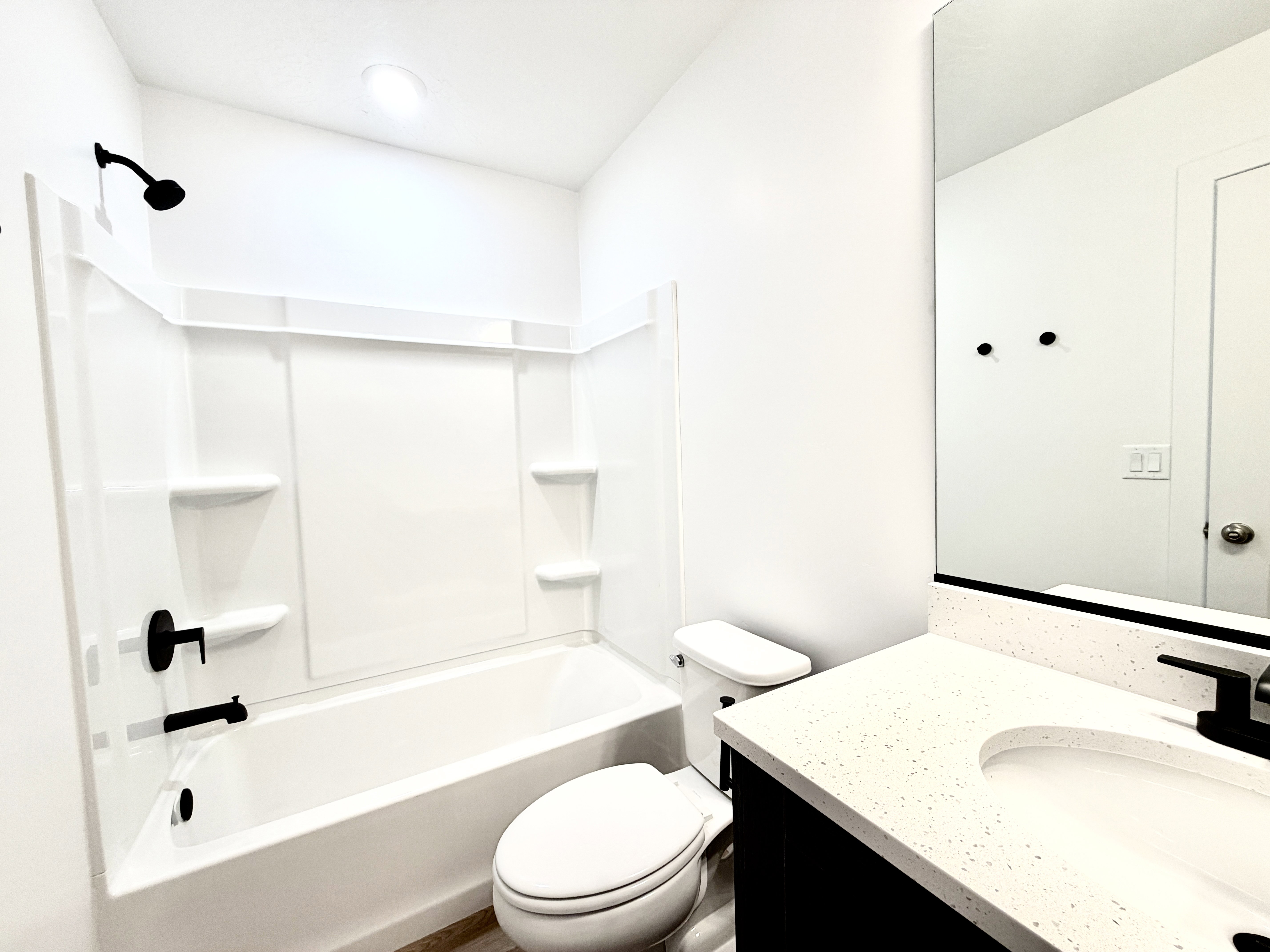 Bathroom featuring a white tub/shower combination, black plumbing fixtures, a white toilet, and a vanity with a white speckled countertop and integrated sink