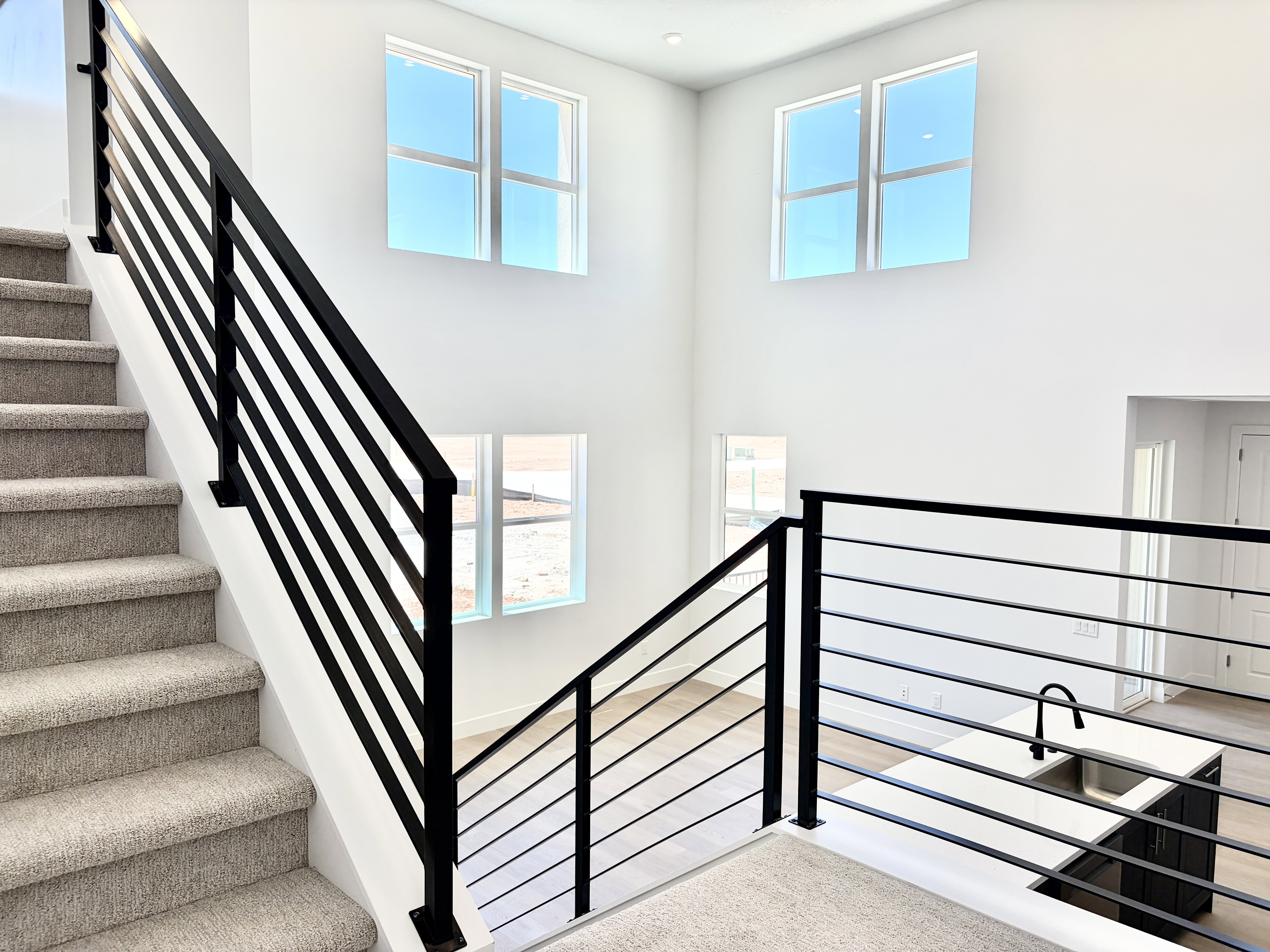 Staircase featuring dark metal horizontal railings and light-colored carpeted treads