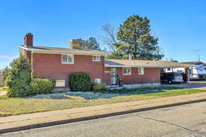 Split level home with an attached carport, brick siding, a chimney, and a front yard