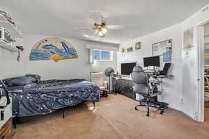 Carpeted bedroom with an office area, a textured ceiling, and a ceiling fan