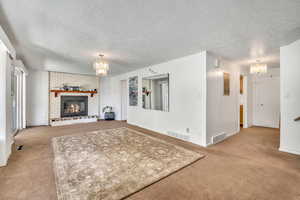 Living room featuring hanging lights, a textured ceiling, light carpet, and a fireplace