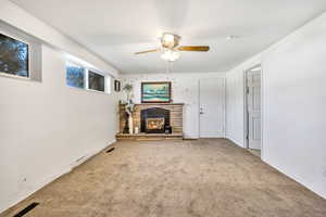 Unfurnished living room with ceiling fan, carpet, and a stone fireplace