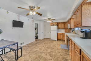 Kitchen featuring light countertops, freestanding refrigerator, wood finish cabinetry, ceiling fan, and black dishwasher