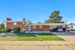 Split level home with brick siding, a chimney, driveway, an attached carport, and a front yard
