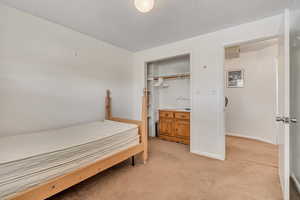 Bedroom with light carpet, a textured ceiling, and a closet