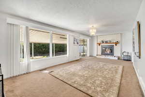 Carpeted living area featuring a textured ceiling, a brick fireplace, and a chandelier