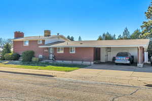 View of front of house featuring brick siding, concrete driveway, a chimney, and roof with shingles