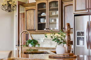 Kitchen featuring stainless steel fridge with ice dispenser, glass fronted cabinets, light stone countertops, backsplash, and a chandelier