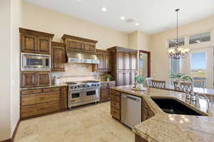 Kitchen featuring stainless steel appliances, ventilation hood, a chandelier, and light stone counters