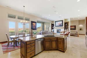 Kitchen with light stone counters, stainless steel dishwasher, a center island with sink, a glass covered fireplace, and open floor plan