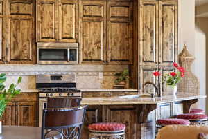 Kitchen with stainless steel appliances, light stone countertops, tasteful backsplash, and a kitchen bar
