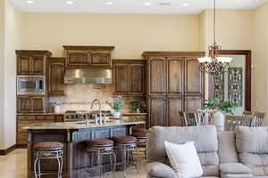 Kitchen with light stone countertops, a kitchen island with sink, hanging lights, a kitchen breakfast bar, and stainless steel microwave