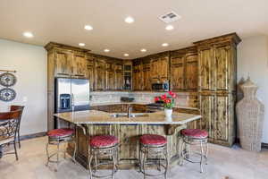 Kitchen featuring glass fronted cabinets, backsplash, light stone counters, a breakfast bar, and stainless steel appliances