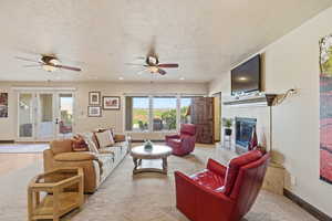 Living area featuring a fireplace, a textured ceiling, french doors, ceiling fan, and light carpet