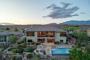 Rear view of house featuring an in-ground hot tub, a balcony, stucco siding, a patio, and a fenced backyard