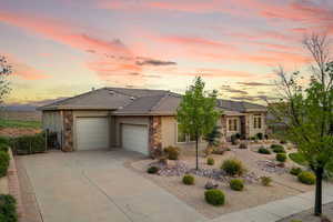 View of front facade with stone siding, an attached garage, driveway, stucco siding, and solar panels