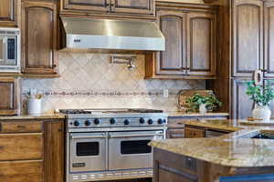 Kitchen with light stone counters, stainless steel appliances, dark wood finish cabinets, and tasteful backsplash