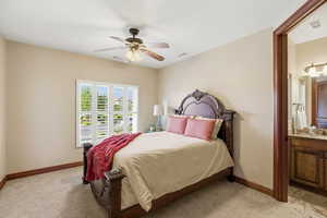 Bedroom featuring light carpet, ceiling fan, and ensuite bath