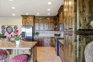 Kitchen with a kitchen bar, stainless steel appliances, glass fronted cabinets, light stone counters, and decorative backsplash