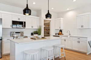 Kitchen featuring a kitchen island, stainless steel appliances, white cabinets, and a kitchen bar