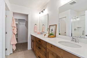 Bathroom featuring double vanity, a spacious closet, a stall shower, and light tile patterned flooring