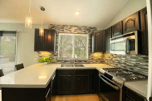 Kitchen featuring a peninsula, stainless steel appliances, light countertops, decorative light fixtures, and light wood-style floors