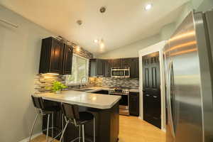 Kitchen with stainless steel appliances, a breakfast bar area, vaulted ceiling, light countertops, and a peninsula