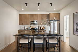 Kitchen featuring wood finish cabinets, a kitchen bar, dark wood-style floors, and stainless steel appliances