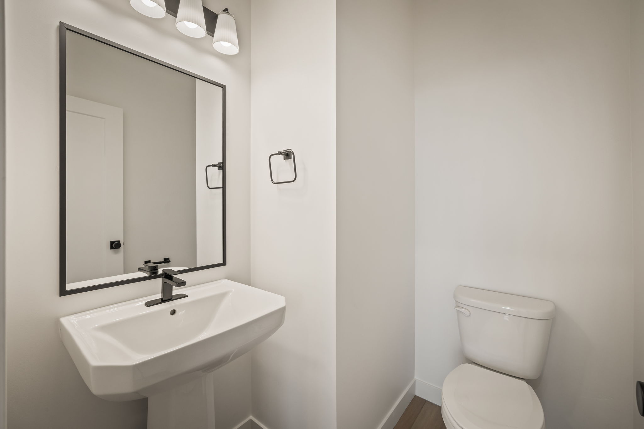 Pedestal sink with a matte black faucet and coordinating rectangular mirror