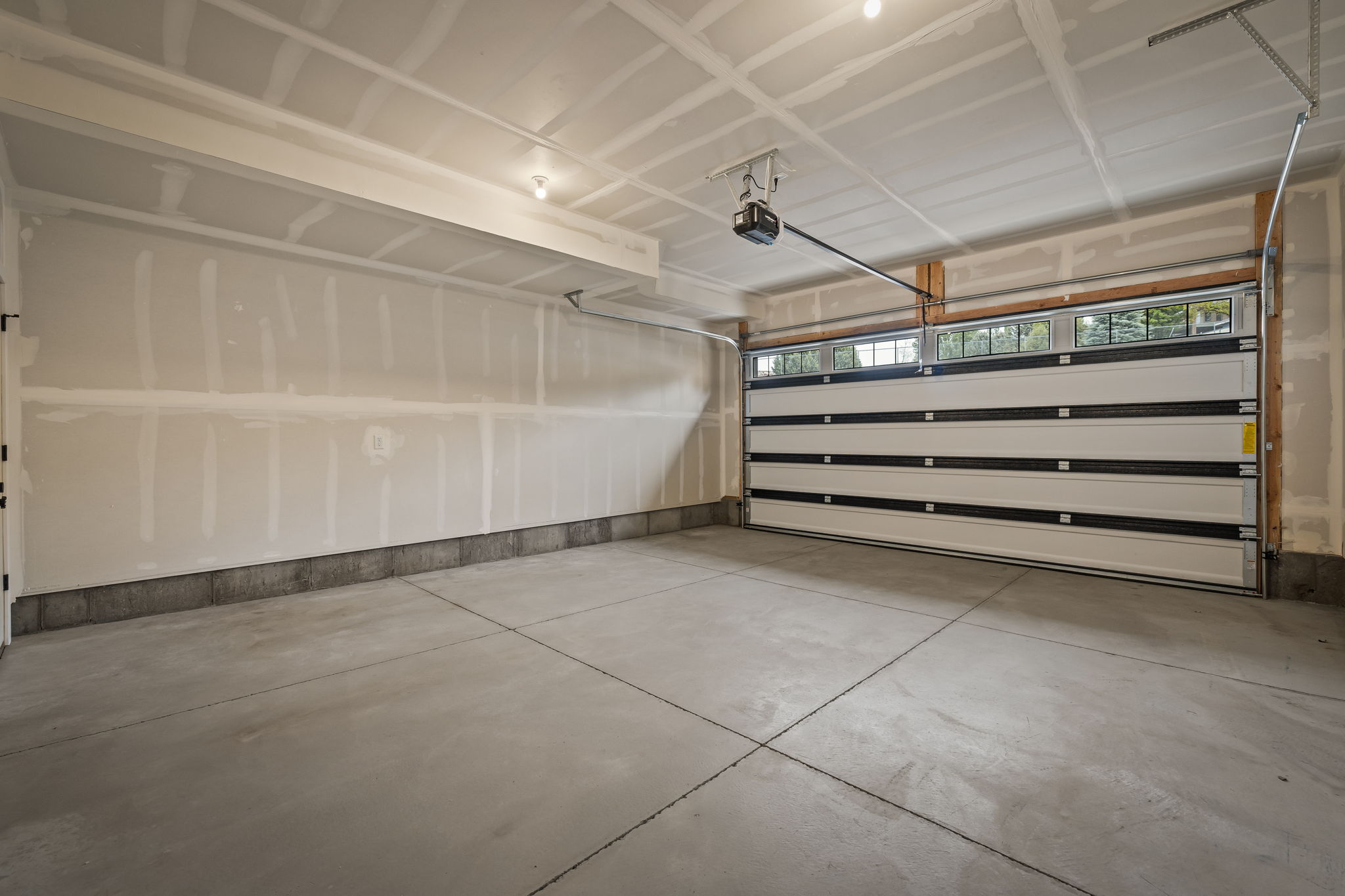 Spacious garage with concrete flooring, automatic garage door opener, and a garage door featuring upper window panels