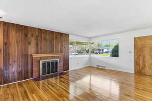 Unfurnished living room featuring a brick fireplace, light wood finished floors, and a textured ceiling