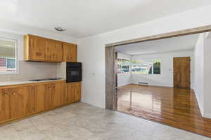 Kitchen with light countertops, wood finish cabinets, black oven, electric cooktop, and light tile patterned flooring