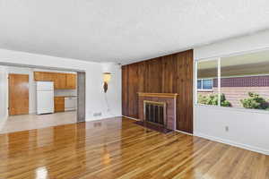 Unfurnished living room with light wood-style flooring, a brick fireplace, and a textured ceiling