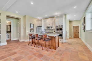 Kitchen with stainless steel appliances, an island with sink, a breakfast bar, light stone counters, and decorative backsplash