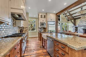 Dual tone kitchen with open floor plan, a stone fireplace, dark wood-type flooring, light stone countertops, and built in appliances