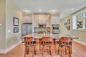 Kitchen with stainless steel appliances, a kitchen island with sink, light stone counters, tasteful backsplash, and recessed lighting