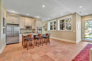 Kitchen with stainless steel appliances, light stone countertops, a kitchen island with sink, a kitchen breakfast bar, and light tile patterned floors