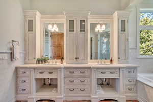 Bathroom featuring double vanity, suspended lighting, tile walls, a garden tub, and a wainscoted wall