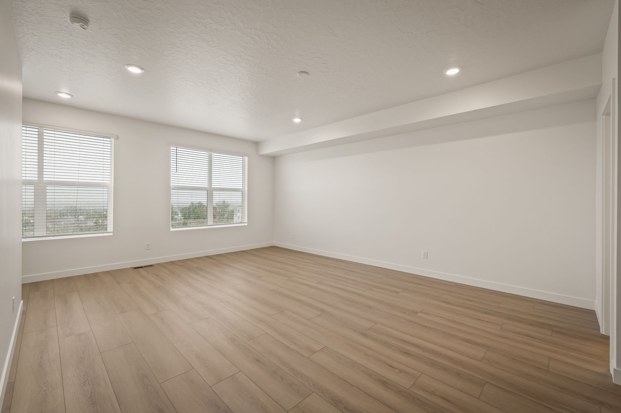 Spacious room featuring light wood-finish flooring, recessed lighting, and multiple windows with blinds