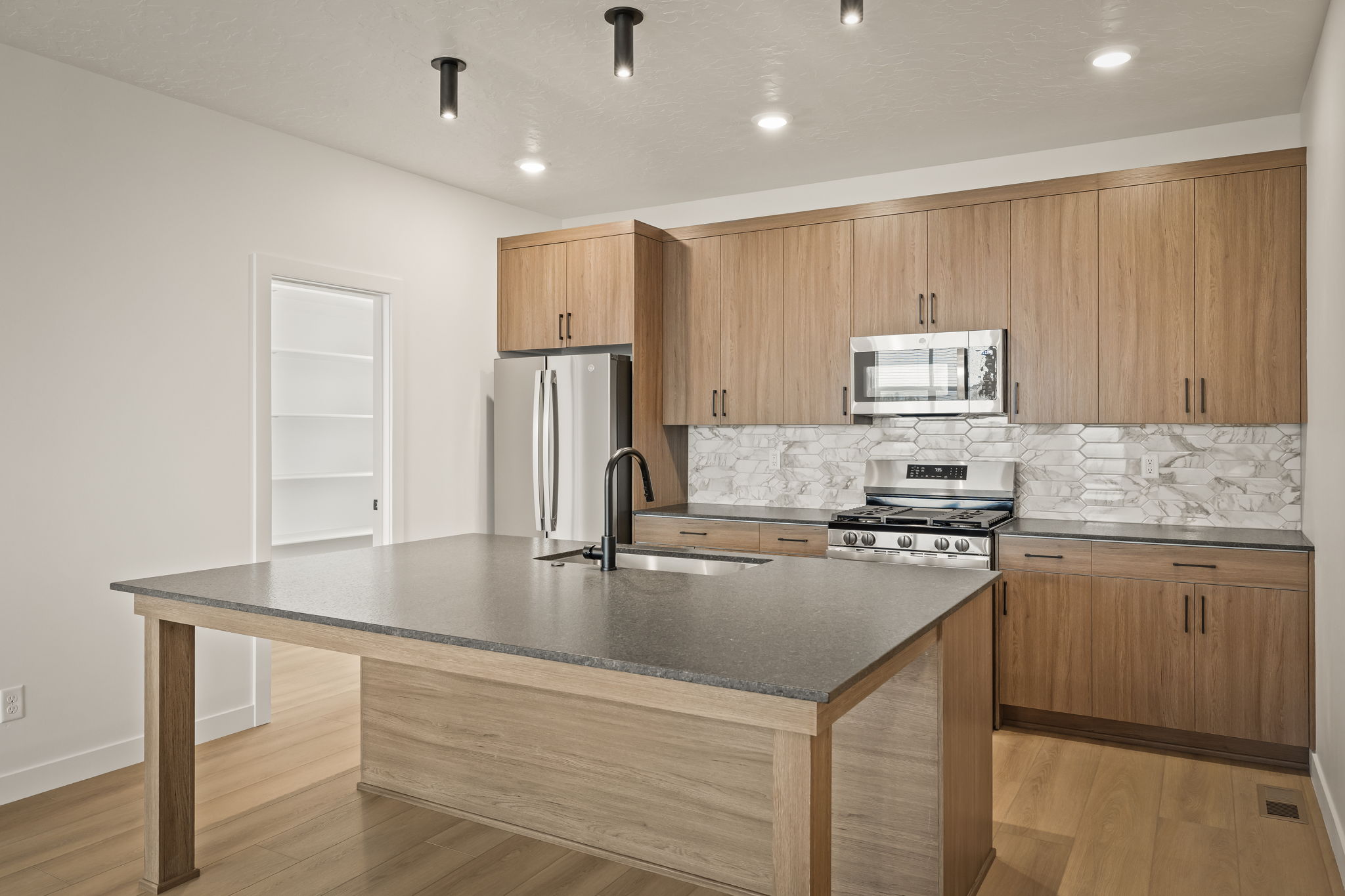 Modern kitchen featuring an island with integrated sink, wood-finish cabinetry, stainless steel appliances, and a patterned tile backsplash