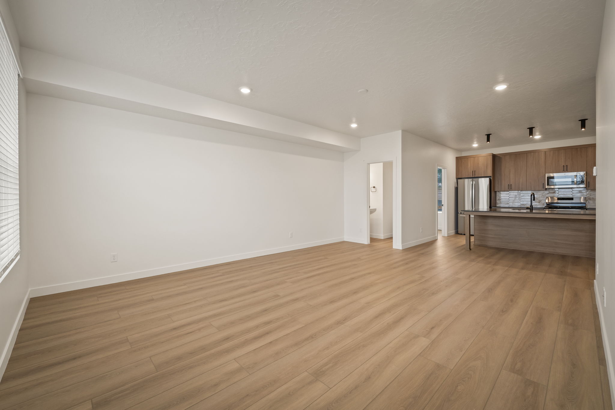 Open-concept living area with wood-finish flooring, recessed lighting, and a kitchen featuring wood cabinetry, stainless steel appliances, and a breakfast bar with a black faucet