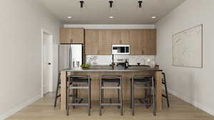 Photos coming soon! - Rending shown. Kitchen with a center island with sink, stainless steel appliances, light wood-style flooring, a kitchen bar, and decorative backsplash