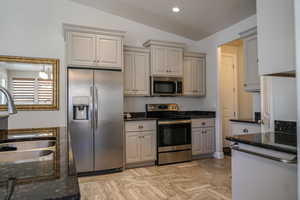 Kitchen featuring stainless steel appliances, vaulted ceiling, dark stone counters, recessed lighting, and gray cabinets