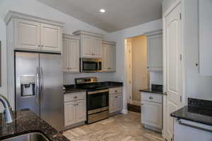 Kitchen with stainless steel appliances, vaulted ceiling, dark stone counters, gray cabinets, and recessed lighting