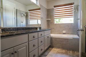 Full bathroom with double vanity, plenty of natural light, dark stone finish flooring, and tiled shower / bath combo