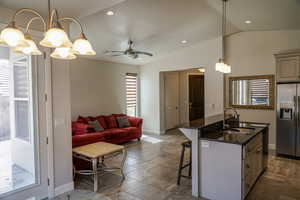Kitchen with a breakfast bar, dark stone countertops, stainless steel appliances, a kitchen island with sink, and decorative light fixtures