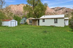 Back of house with a storage shed, a lawn, a mountain view, concrete block siding, and a metal roof