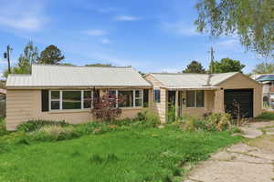 Ranch-style house featuring a metal roof, a garage, a front yard, and driveway